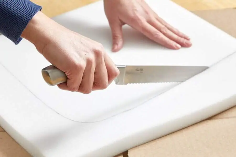 Cutting foam padding with a serrated knife for a furniture reupholstery project.