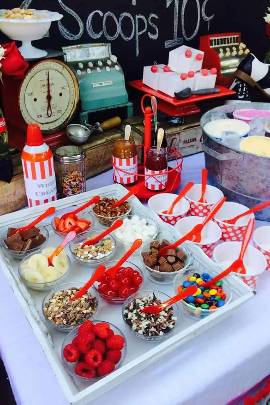 Ice cream bar setup with colorful toppings and vintage decor at an outdoor birthday party.