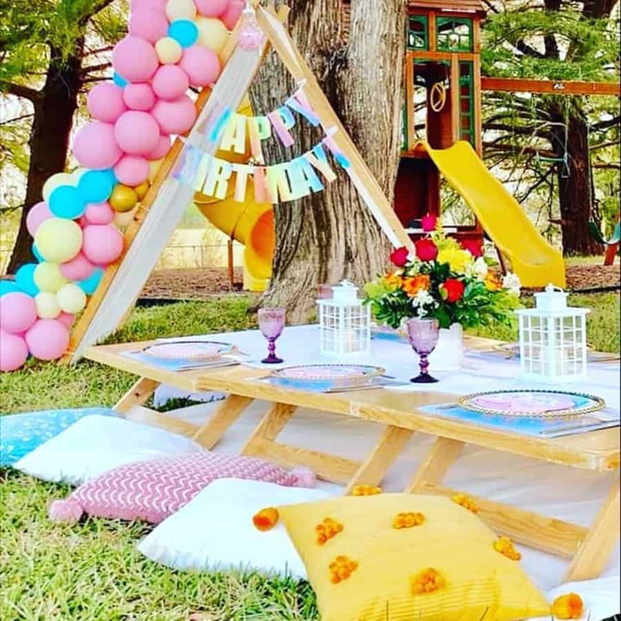 Colorful outdoor kids' birthday setup with balloons, table decor, and play area in the background.