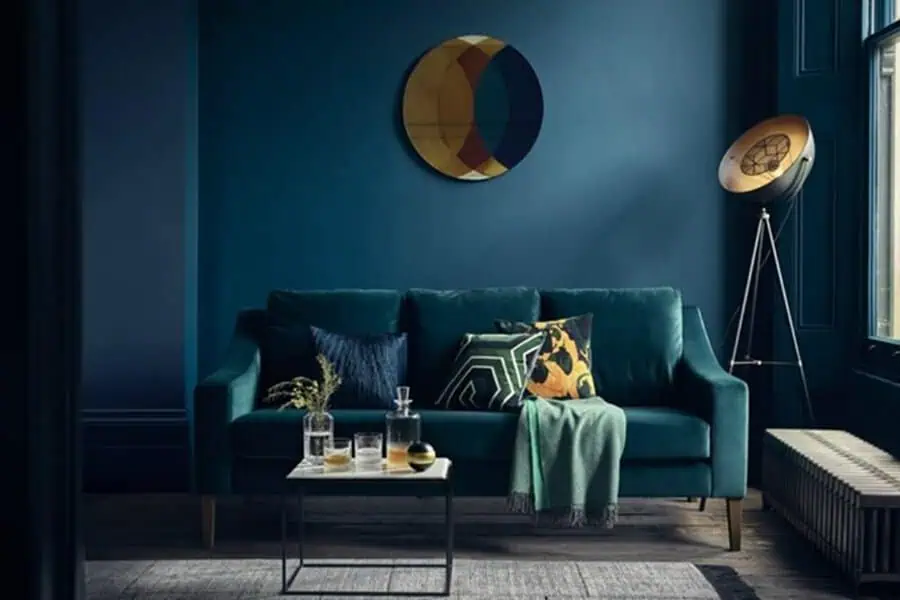 Moody living room with teal layers, geometric pillows, and statement lighting.