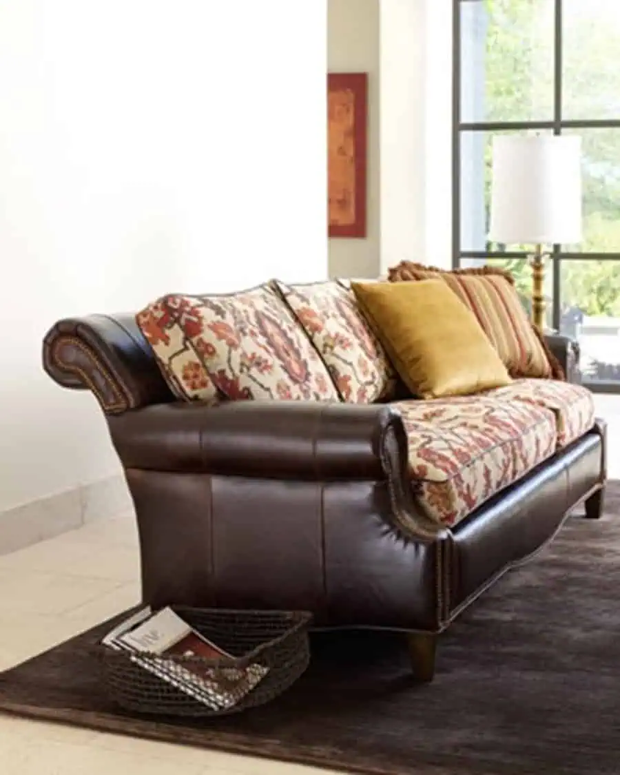 Leather sofa with floral patterned cushions, striped pillows, and a basket on a dark rug.