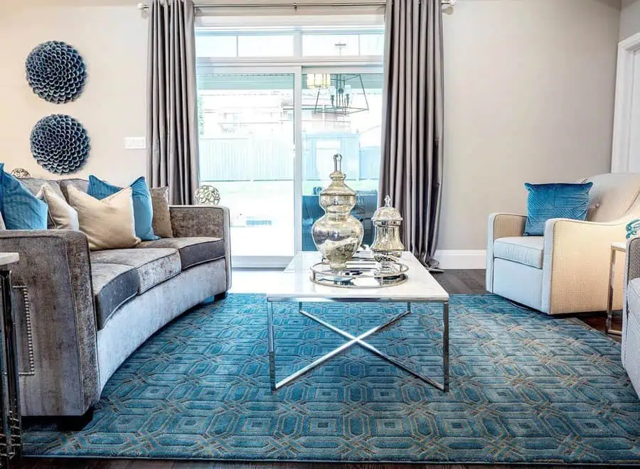 Teal living room with velvet sofa, geometric rug, blue pillows, and silver decorative accents.