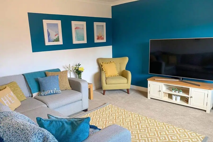 Teal living room with accent wall, gray sofa, yellow armchair, and patterned rug.