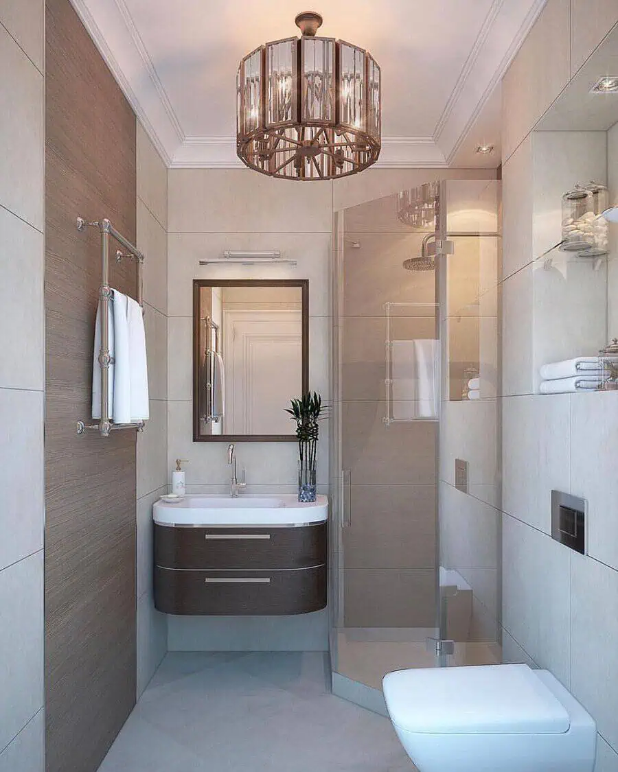 Small luxury bathroom with glass shower, modern vanity, chandelier, and neutral tile design.