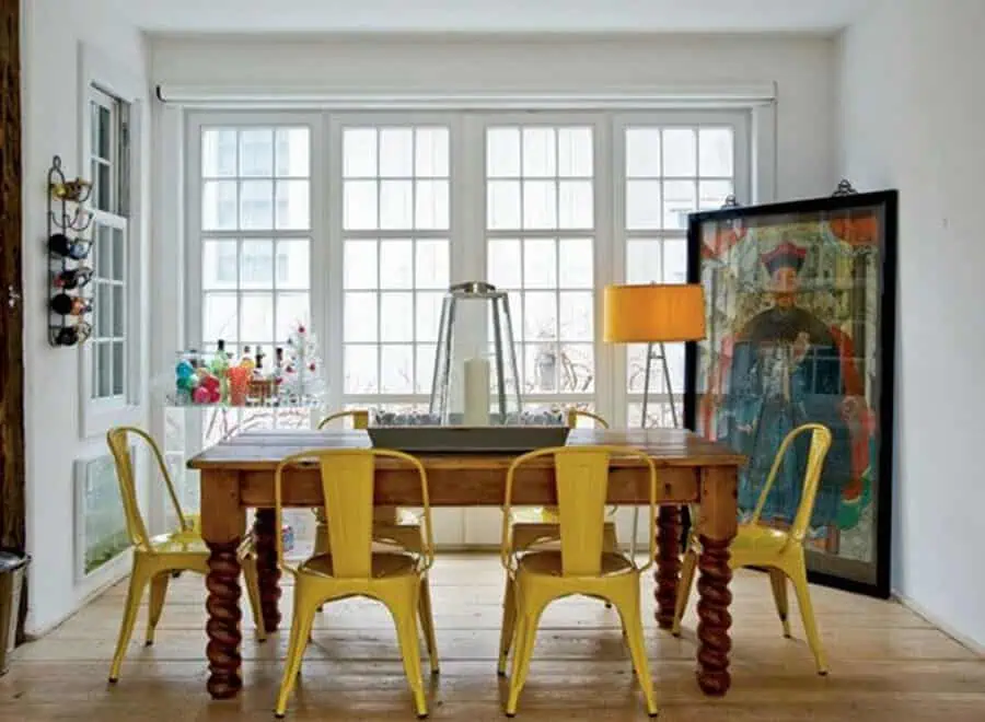 Eclectic dining area with rustic table, yellow chairs, large windows, and artistic decor accents.