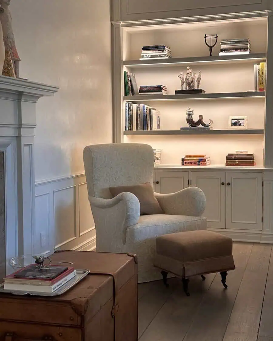 Minimalist den with armchair, ottoman, built-in shelves, and warm ambient lighting.