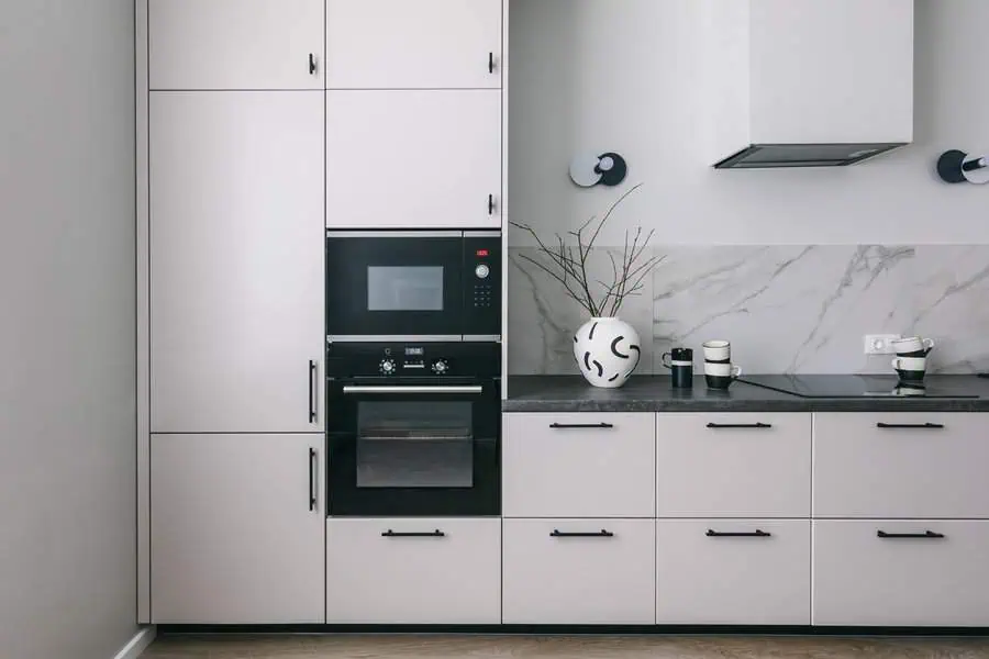 Modern kitchen with white cabinets, black appliances, marble backsplash, and decorative vase.