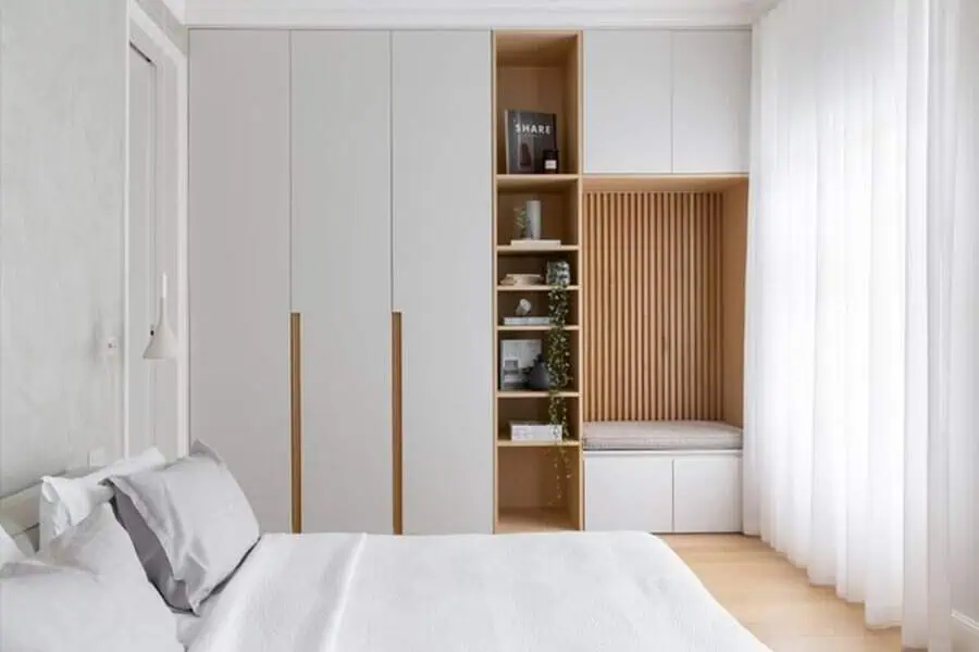 Minimalist bedroom with built-in white wardrobes, wooden shelving, and a cozy reading nook.