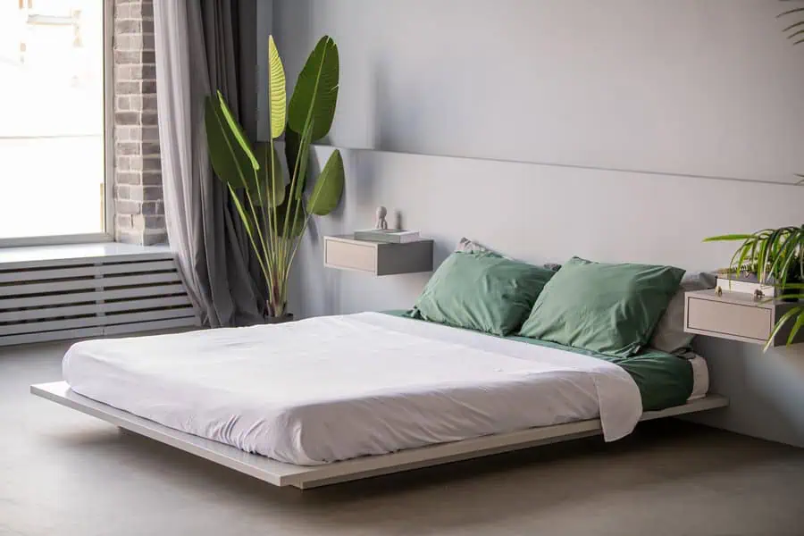 Modern bedroom with a low platform bed, green pillows, and potted plants by the window.