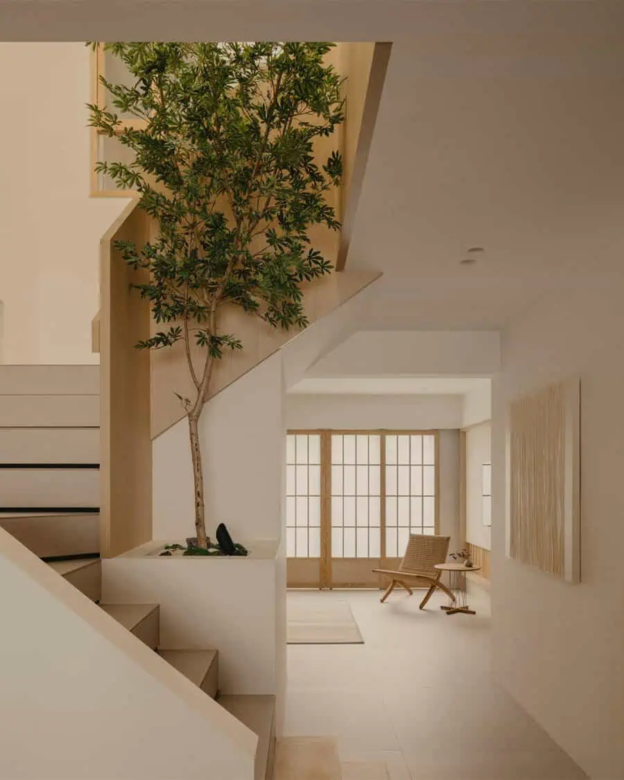 Minimalist interior with a staircase, indoor tree, and a bright Japanese-inspired sitting area.