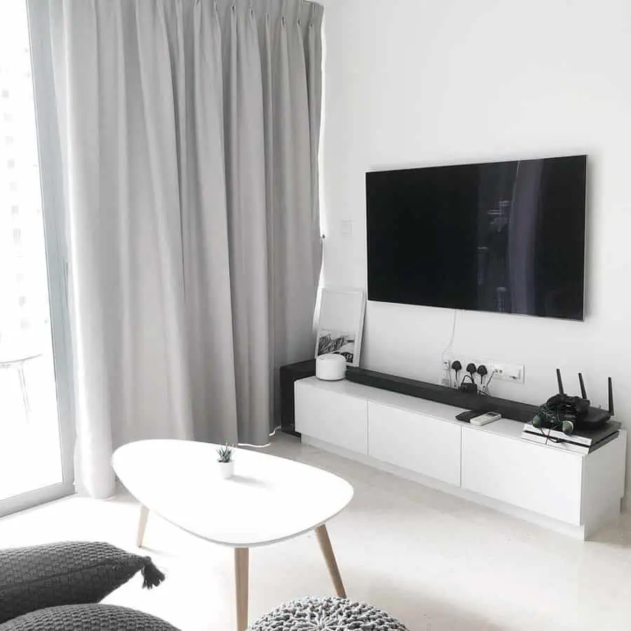 Minimalist living room with white furniture, wall-mounted TV, and grey curtains.