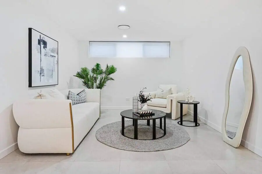 Bright minimalist living room with white furniture, a round mirror, and a modern coffee table.