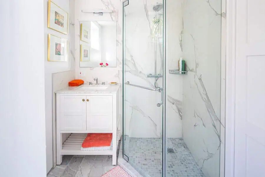 Minimalist small luxury bathroom with marble tiles, glass shower, white vanity, and vibrant accents.