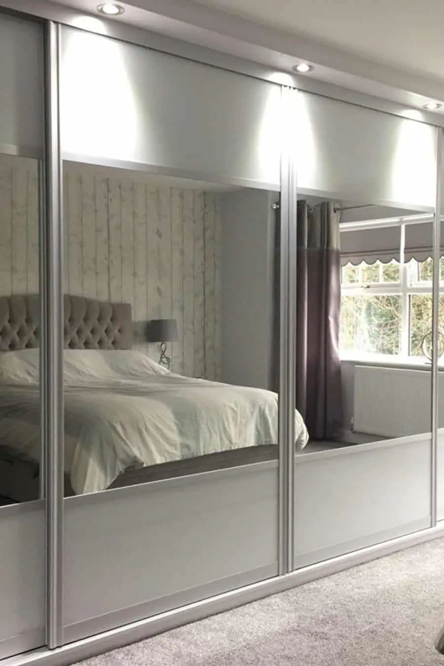 Modern bedroom with mirrored sliding wardrobe, tufted headboard, and soft lighting.