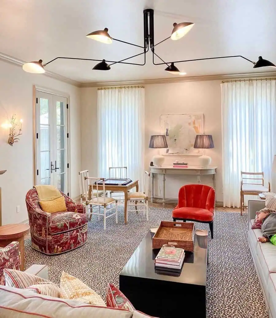 Bright den with modern chandelier, patterned chairs, colorful accents, and natural light.