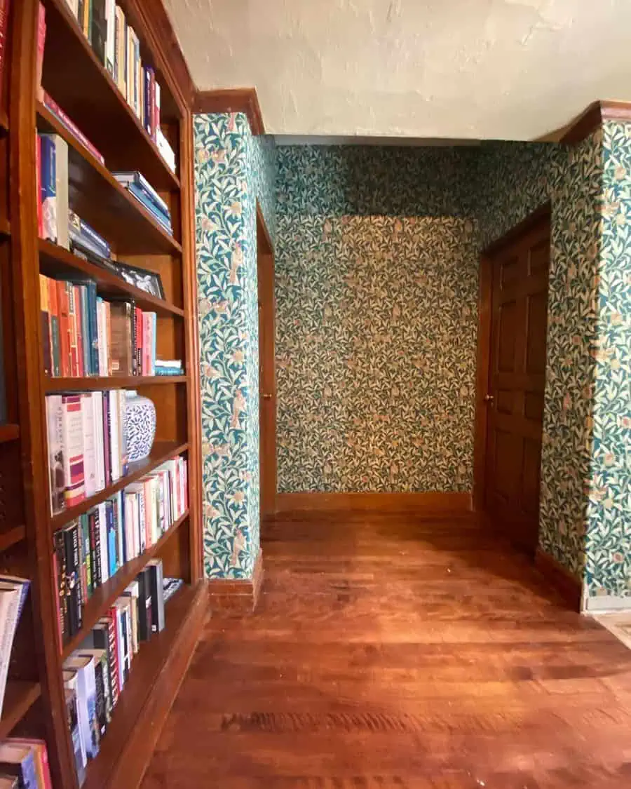 Modern hallway den with floral wallpaper, built-in bookshelves, and wooden flooring.