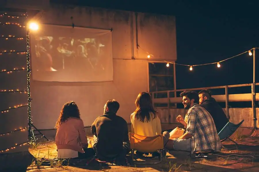 Outdoor movie night birthday party with friends sitting under string lights.