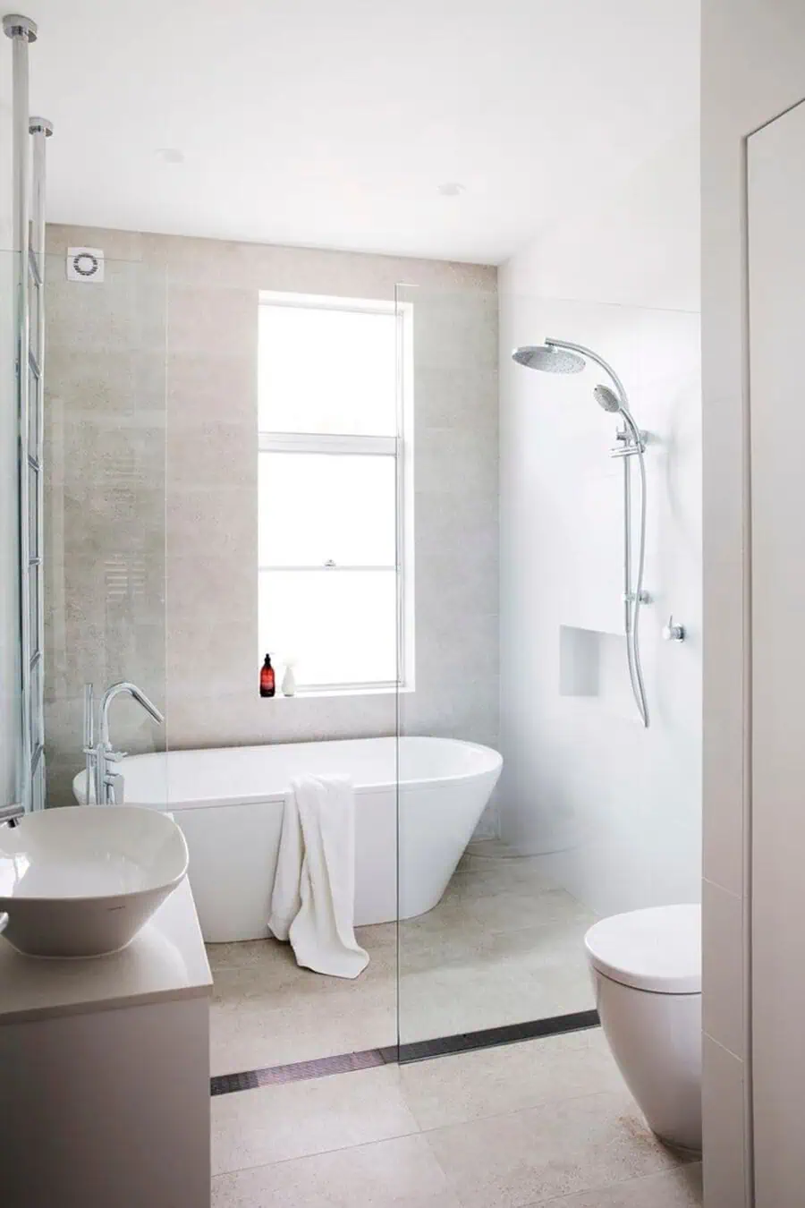 Small luxury bathroom with freestanding tub, glass shower, minimalist fixtures, and natural light.