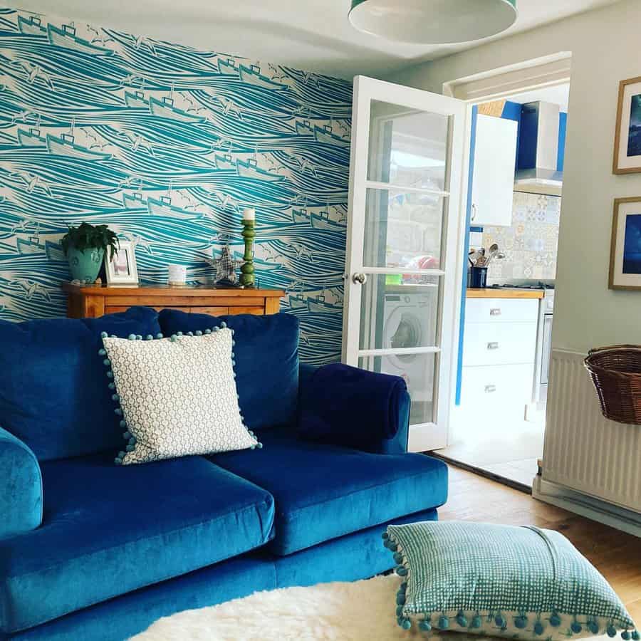 Living room with teal patterned wallpaper, navy blue sofa, white cushion, and open kitchen view.