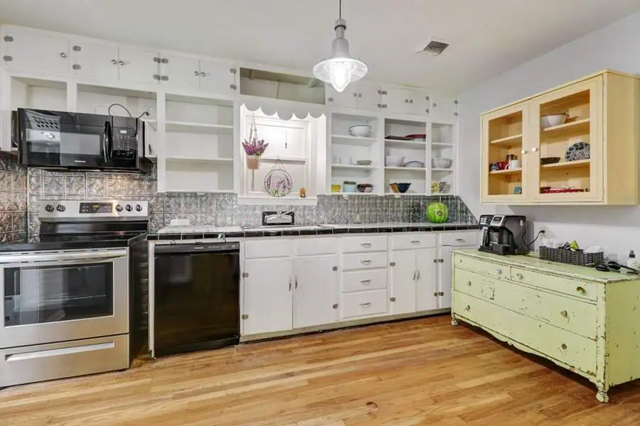 1950s kitchen with open shelving, white cabinets, stainless steel appliances, and wood flooring.