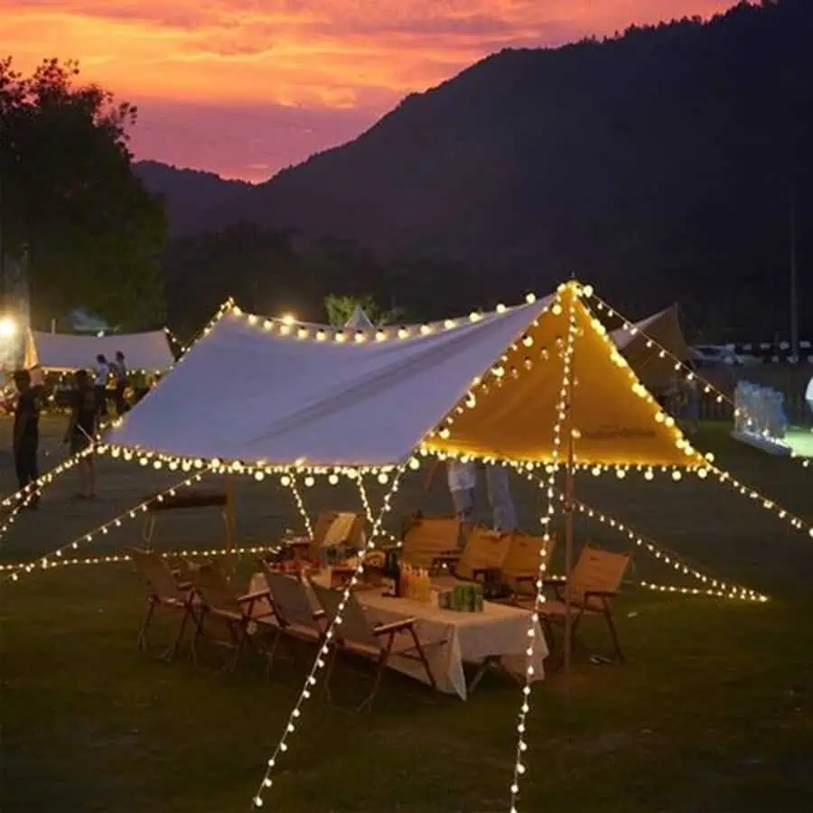 Outdoor birthday party under a tent decorated with string lights at sunset.