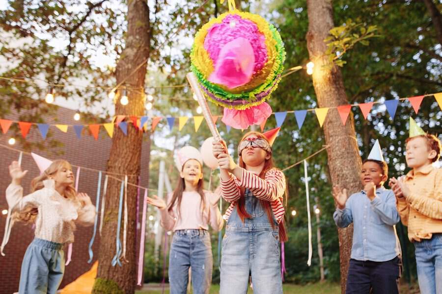 Kids playing a piñata game at a garden birthday party with colorful decorations.