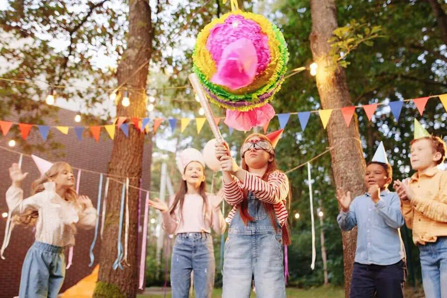 Kids playing a piñata game at a garden birthday party with colorful decorations.