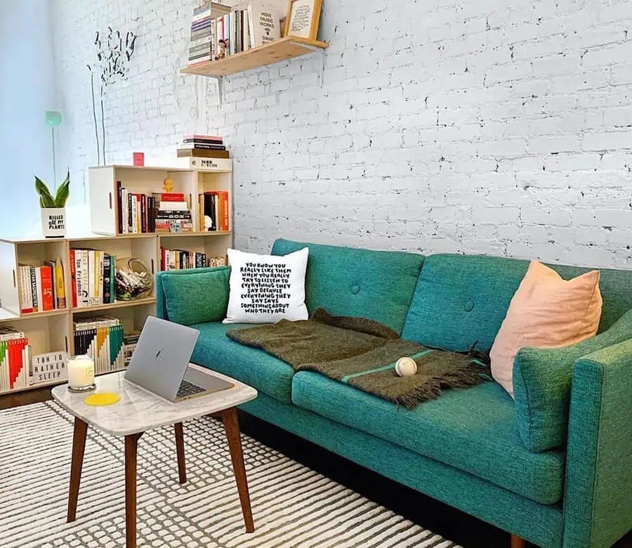 Cozy living room with a teal sofa, pale peach pillow, and a white brick wall backdrop.