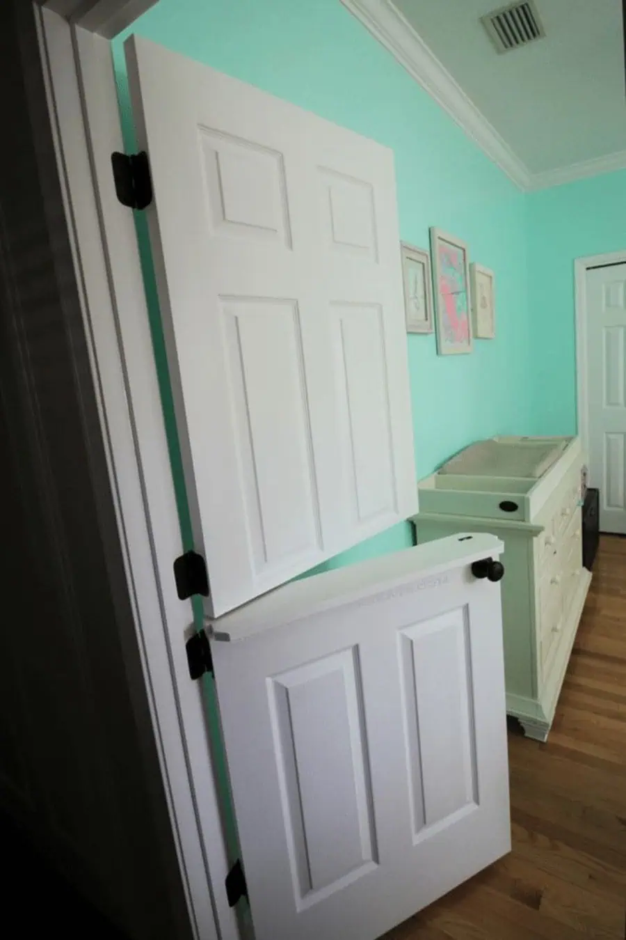 White Dutch door in a mint green room with hardwood flooring and wall decor.