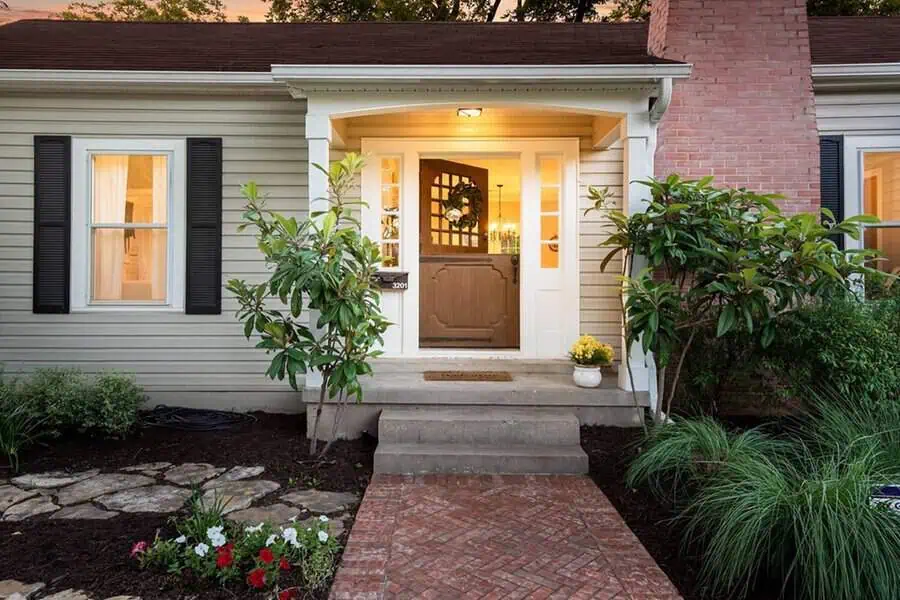 Warm entryway with wooden Dutch door, brick steps, and lush garden landscaping at sunset.