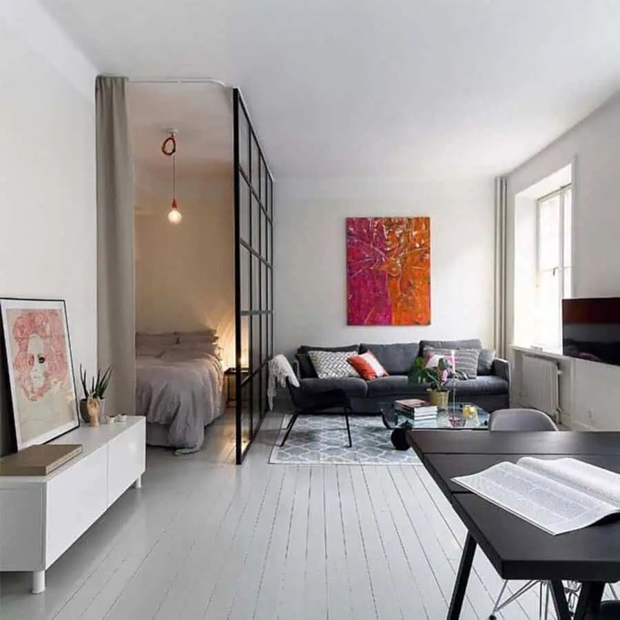 Studio apartment with colorful abstract art, cozy living area, and modern glass bedroom divider.