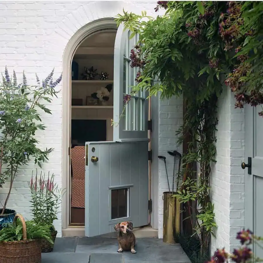 Soft blue Dutch door with a built-in pet door, surrounded by lush greenery and a cozy outdoor setting.