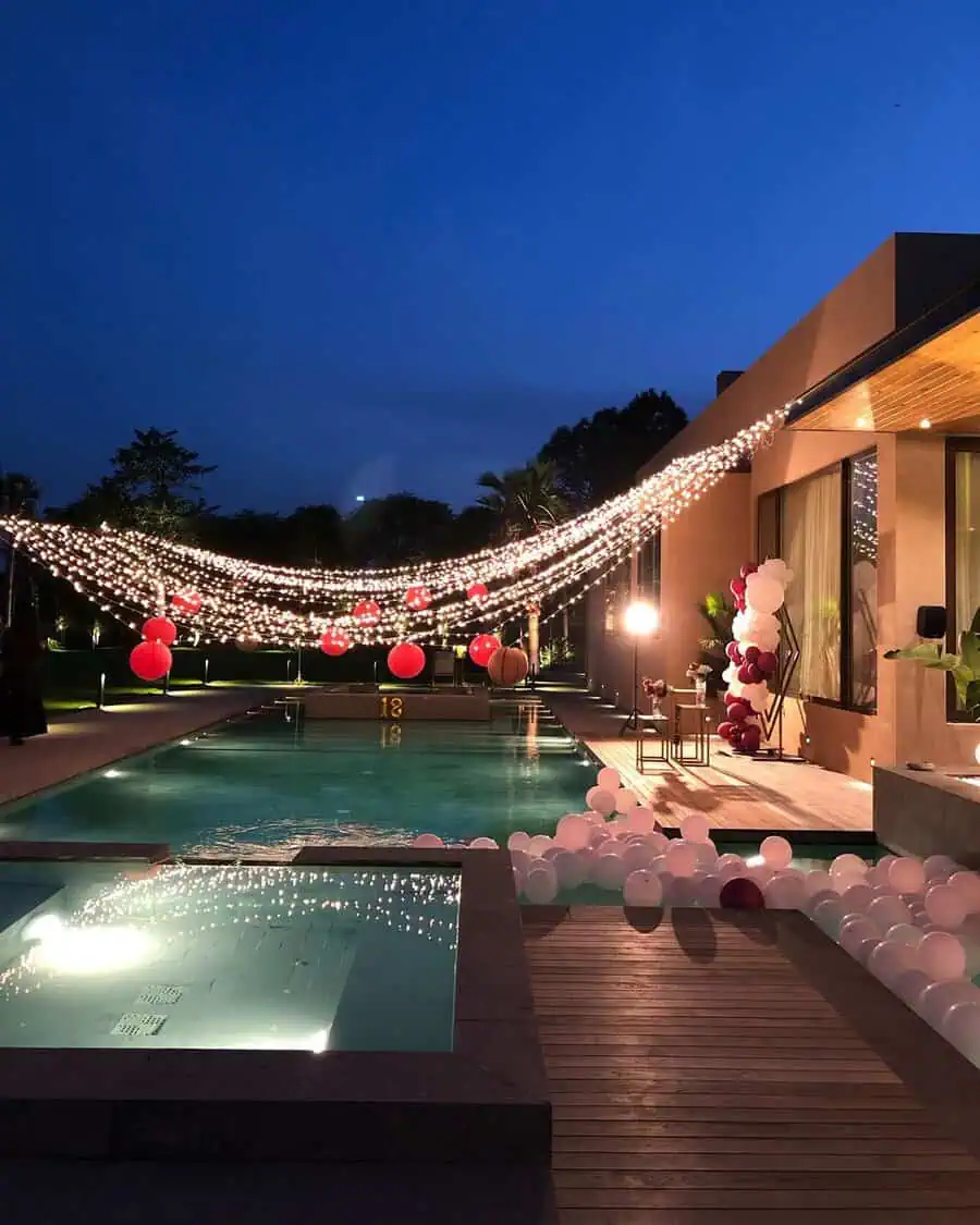 Poolside outdoor birthday party with string lights and balloon decorations at night.