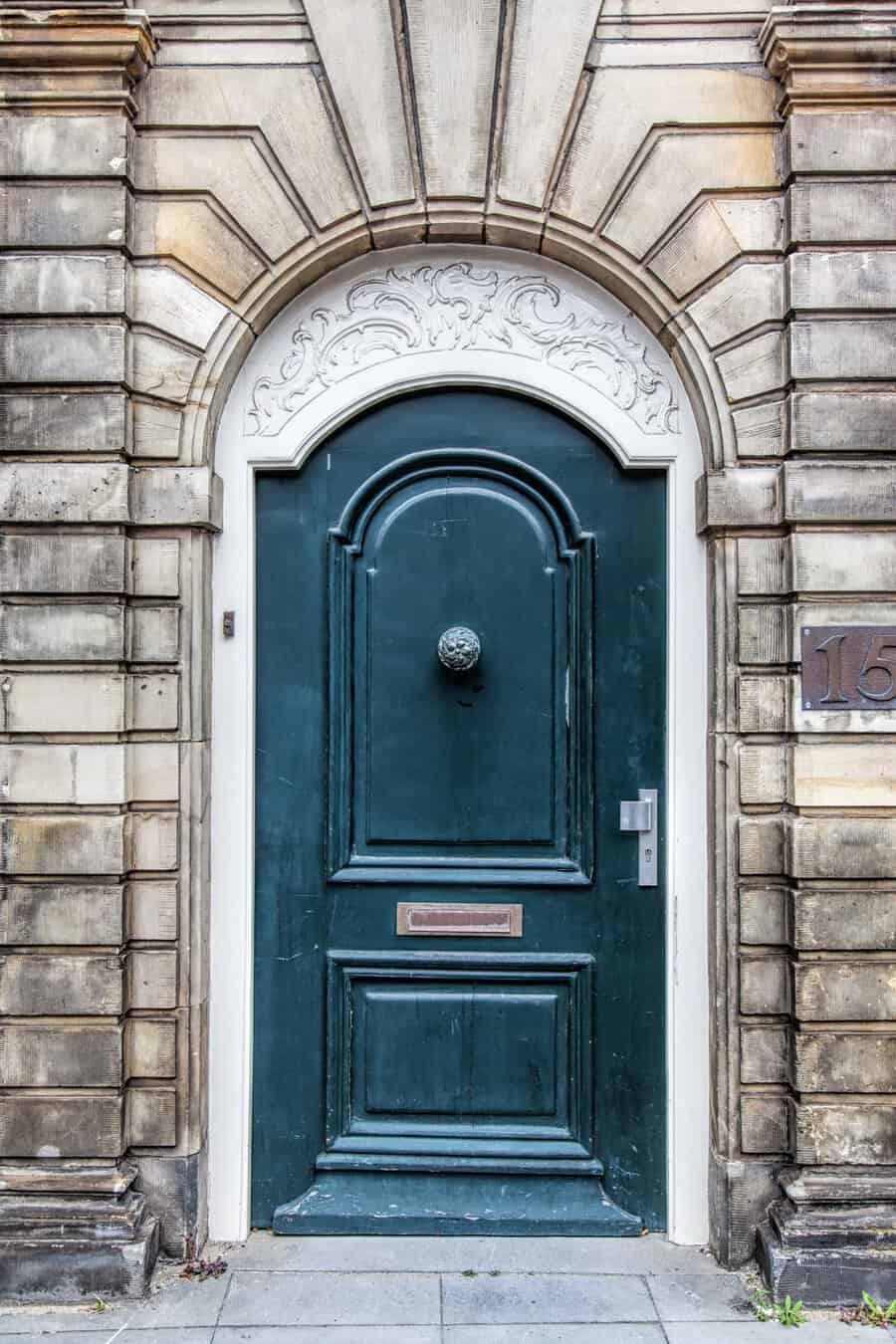 Arched dark green wooden door with ornate carvings and stone surround on a historic building.
