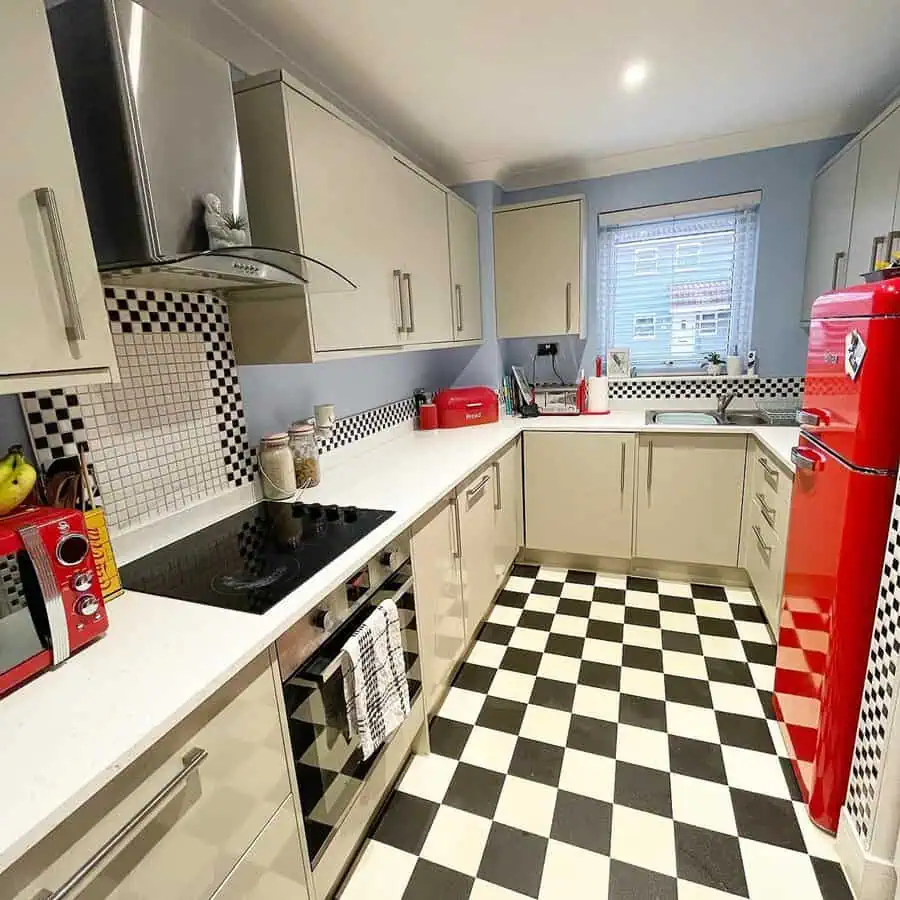 Retro-style kitchen with red appliances, checkerboard floor, and white cabinets.