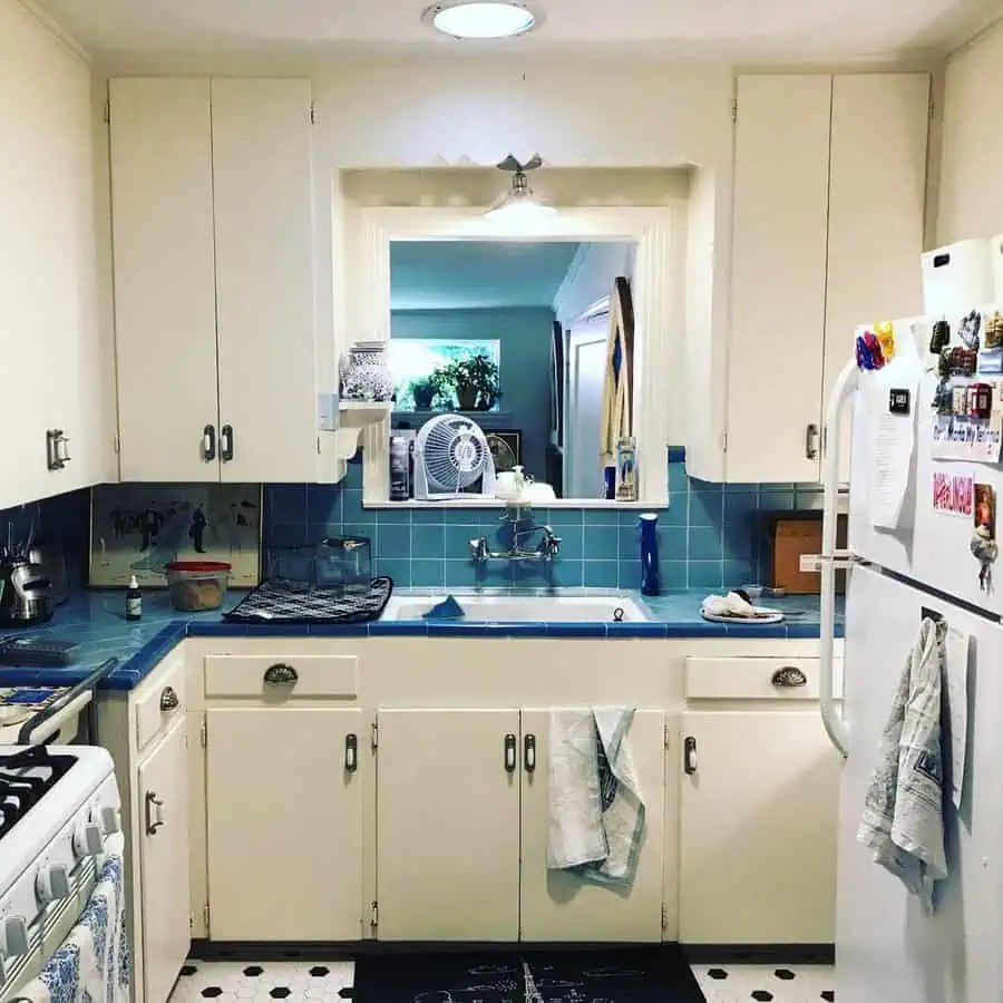 1950s kitchen with blue tile countertops, white cabinets, and retro scalloped lighting.