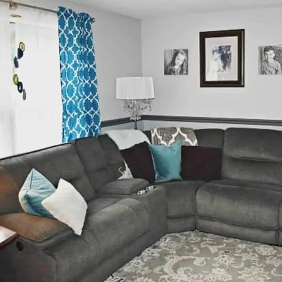 Cozy living room with slate gray sectional, teal pillows, patterned blue curtains, and gray walls.