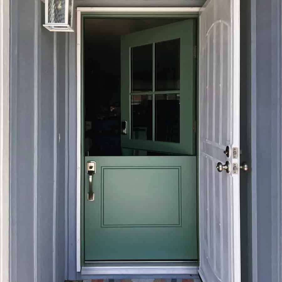 Green Dutch door with glass panes and sleek hardware, set against a gray exterior wall.