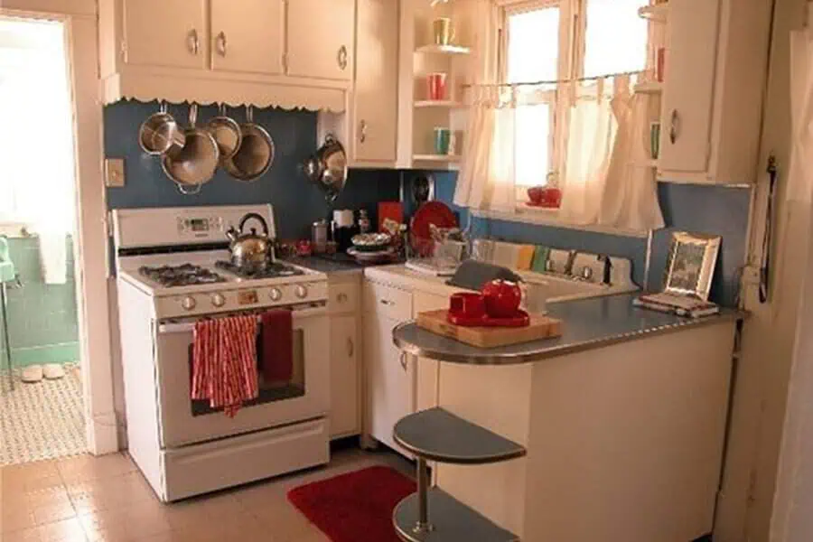 Small 1950s kitchen with blue backsplash, white cabinets, and retro appliances.