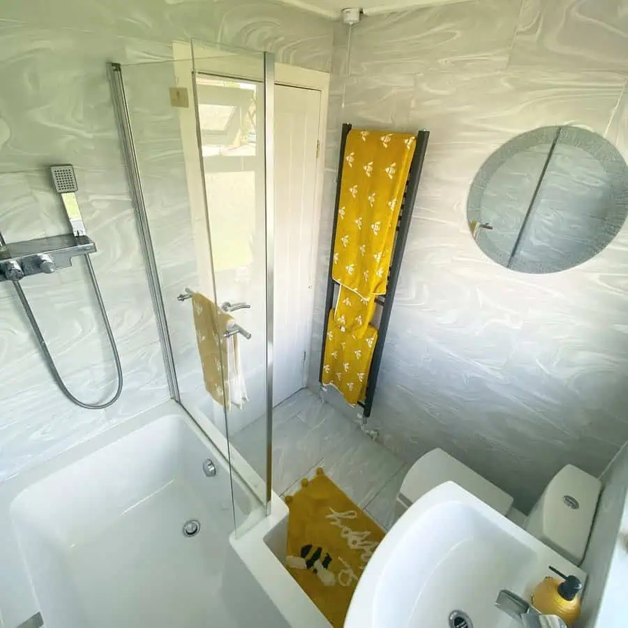 Small bathroom with marble-effect walls, glass shower, yellow accents, and modern fixtures.