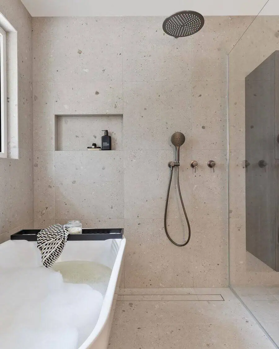 Small luxury bathroom with neutral stone tiles, freestanding tub, rain shower, and built-in niche.