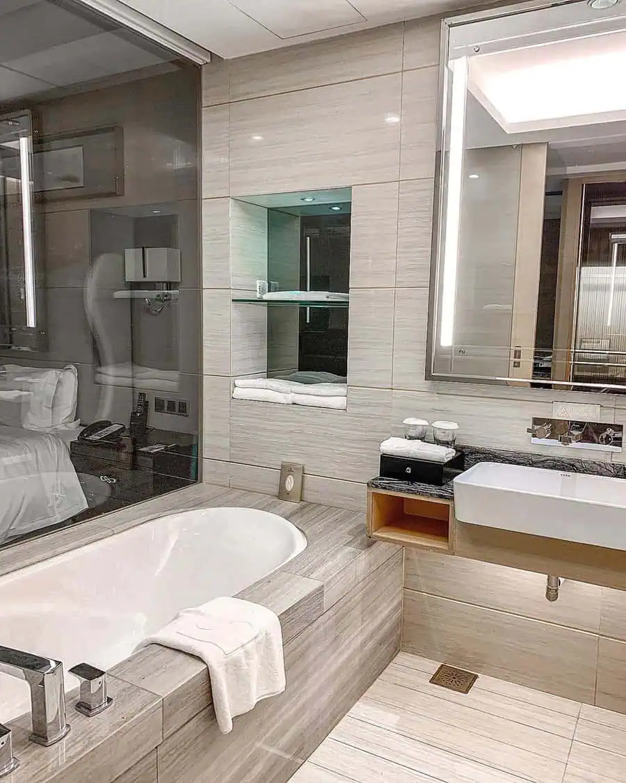 Small luxury bathroom with built-in bathtub, illuminated mirror, and modern storage features.