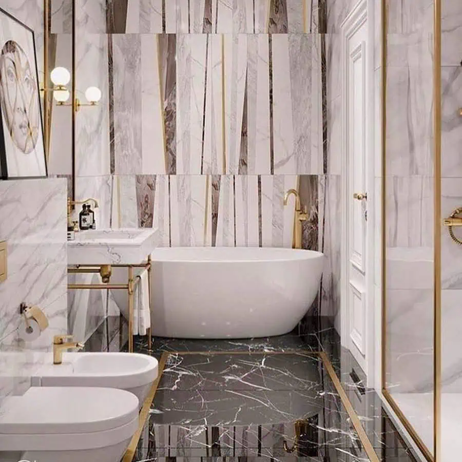 Small luxury bathroom with modern fixtures, marble walls, gold accents, and freestanding tub.