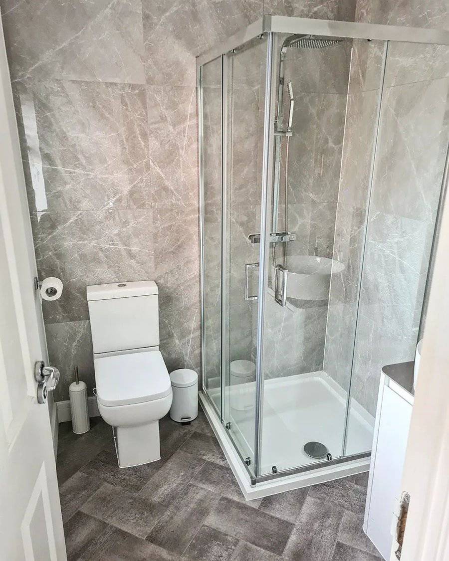 Small luxury bathroom with glass shower enclosure, modern fixtures, and marble-style tiles.