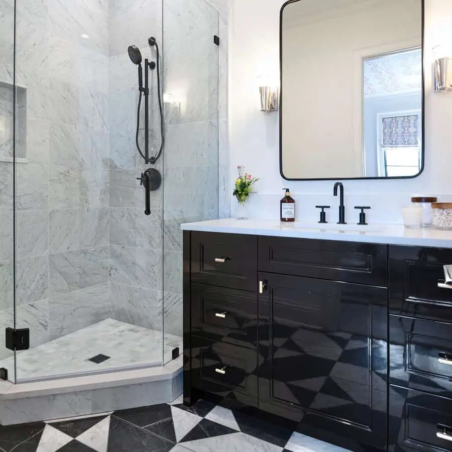 Small luxury bathroom with black vanity, glass shower, marble tiles, and geometric flooring.