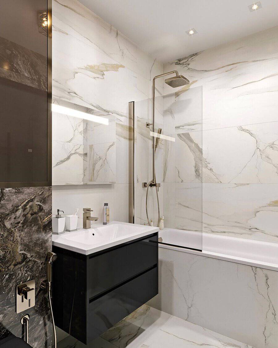 Small luxury bathroom with marble walls, black vanity, glass shower, gold fixtures, and luxe lighting.