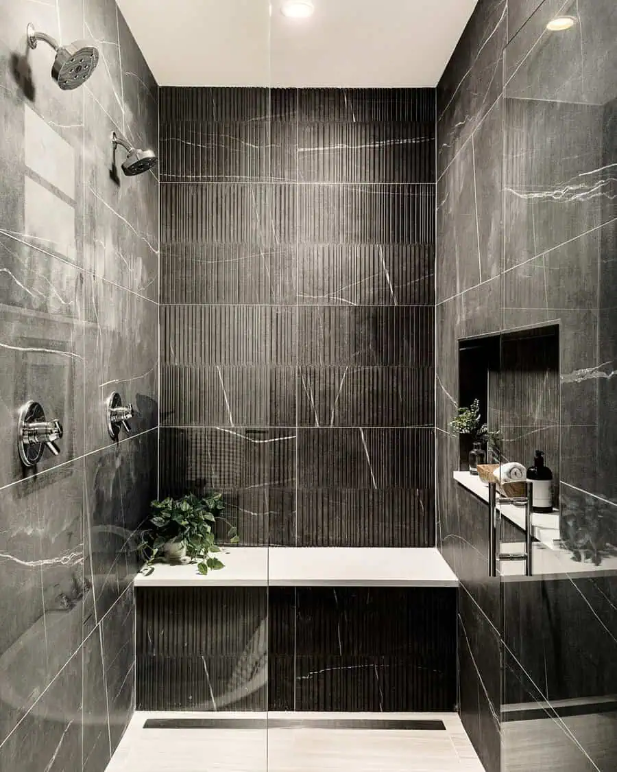 Small luxury bathroom with black textured tiles, dual showerheads, built-in bench, and sleek accessories.