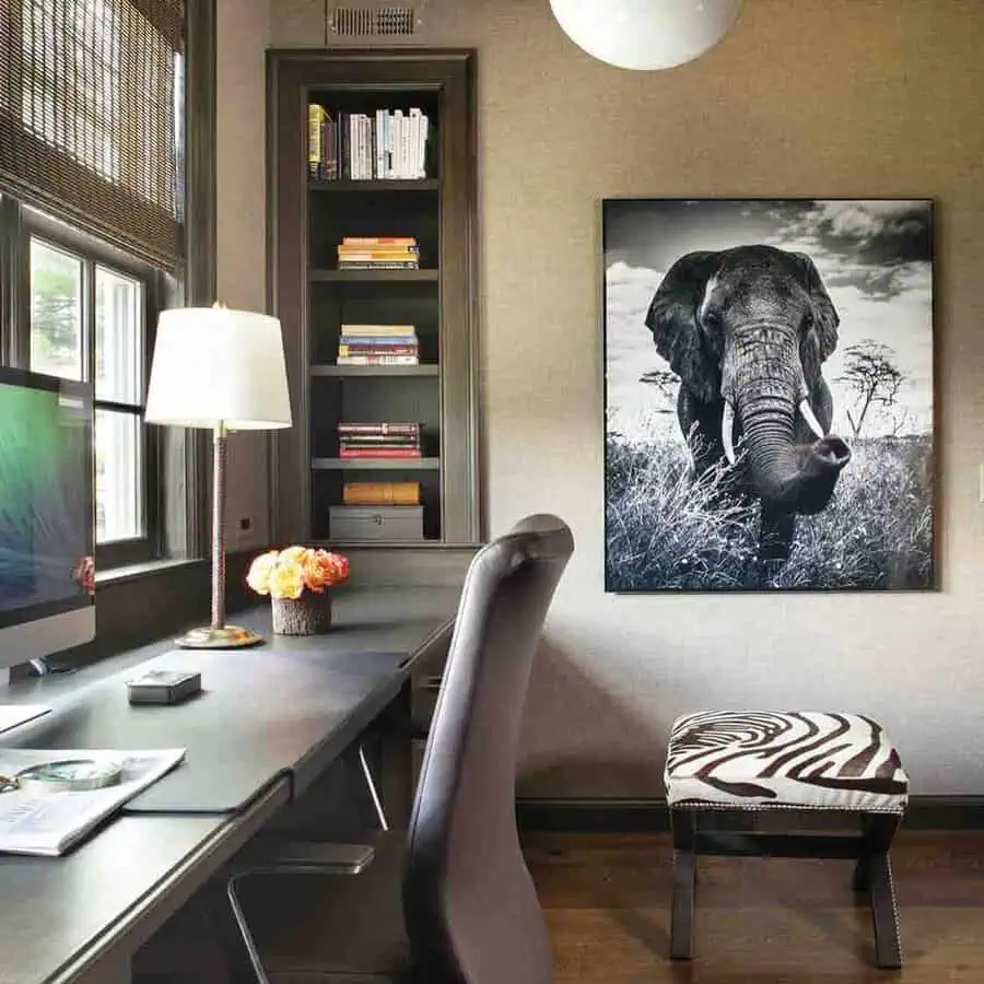 Modern home office with desk, elephant wall art, built-in shelves, and zebra-print stool.