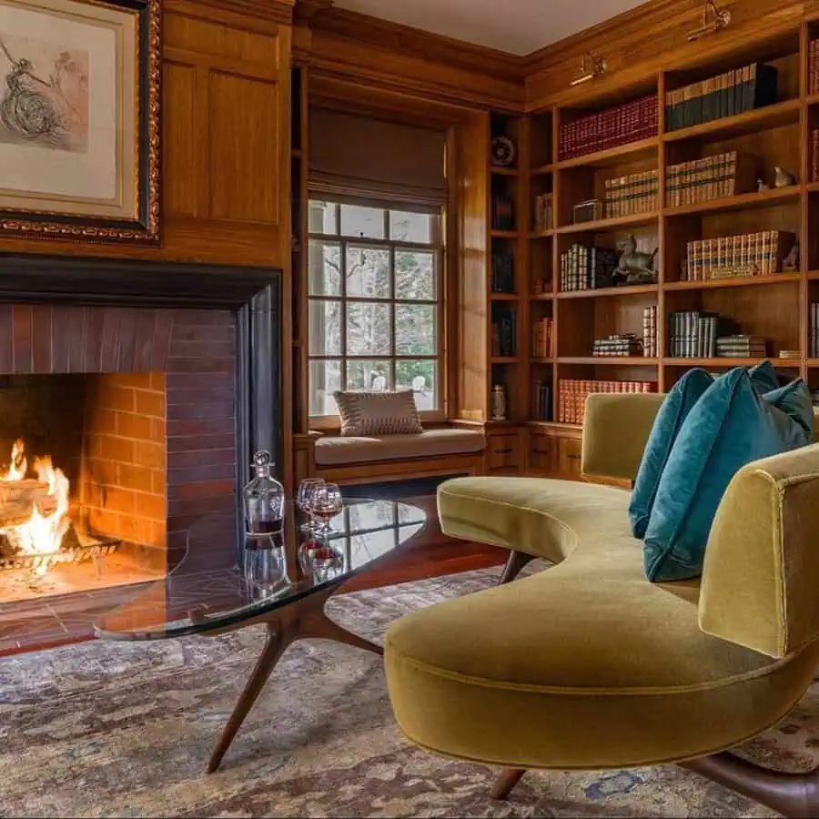 Cozy den with wooden bookshelves, a lit fireplace, curved sofa, and glass coffee table.