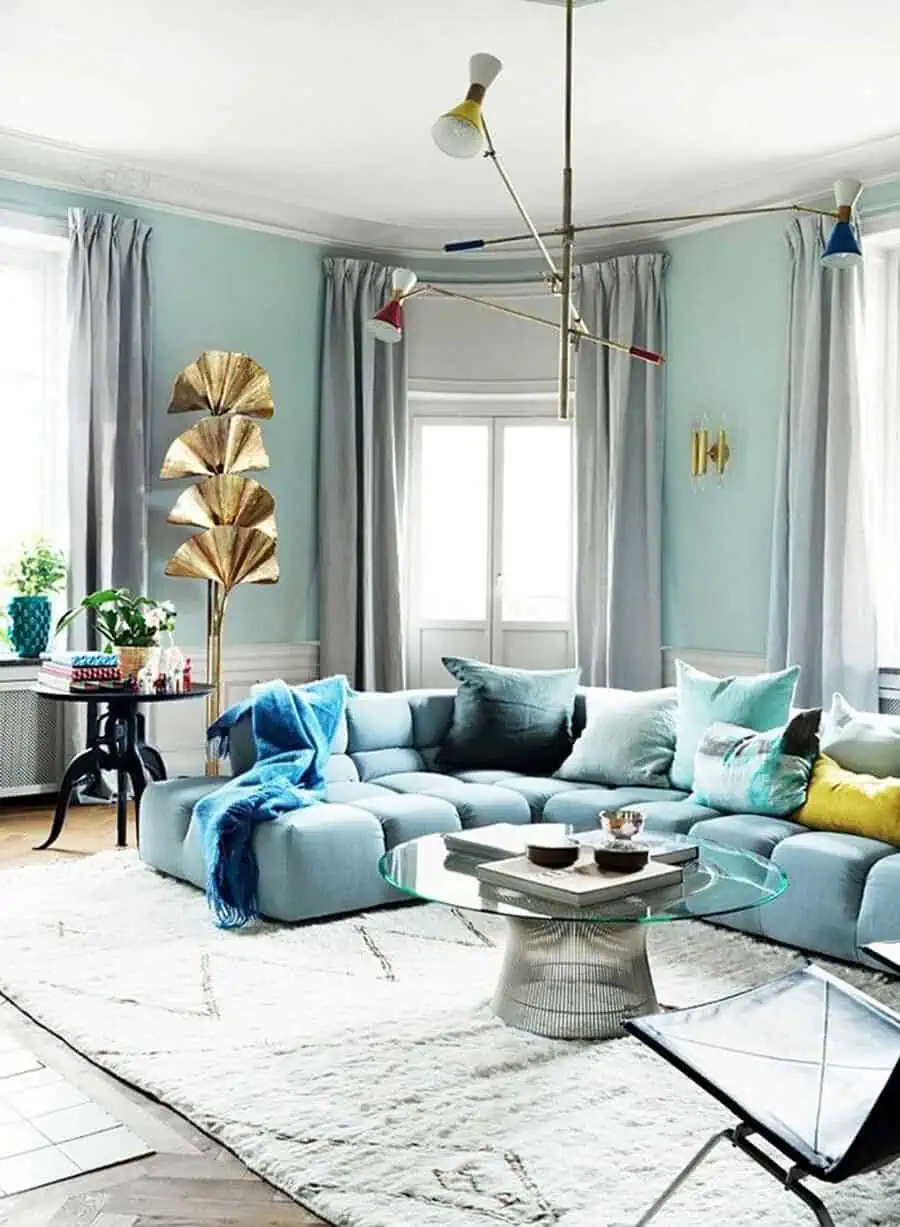 Bright living room with soft mint walls, tufted blue sofa, colorful pillows, and gold decor accents.